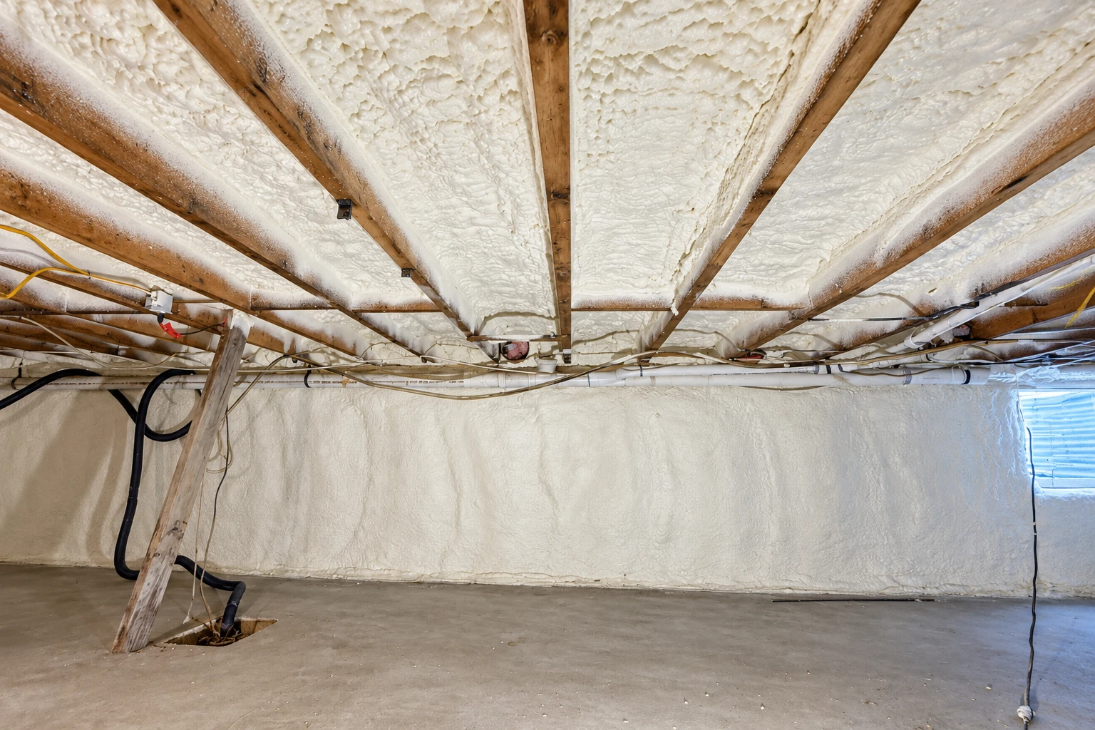 Spray foam insulation coats the underside of a crawl space ceiling and walls around exposed beams and utility lines.