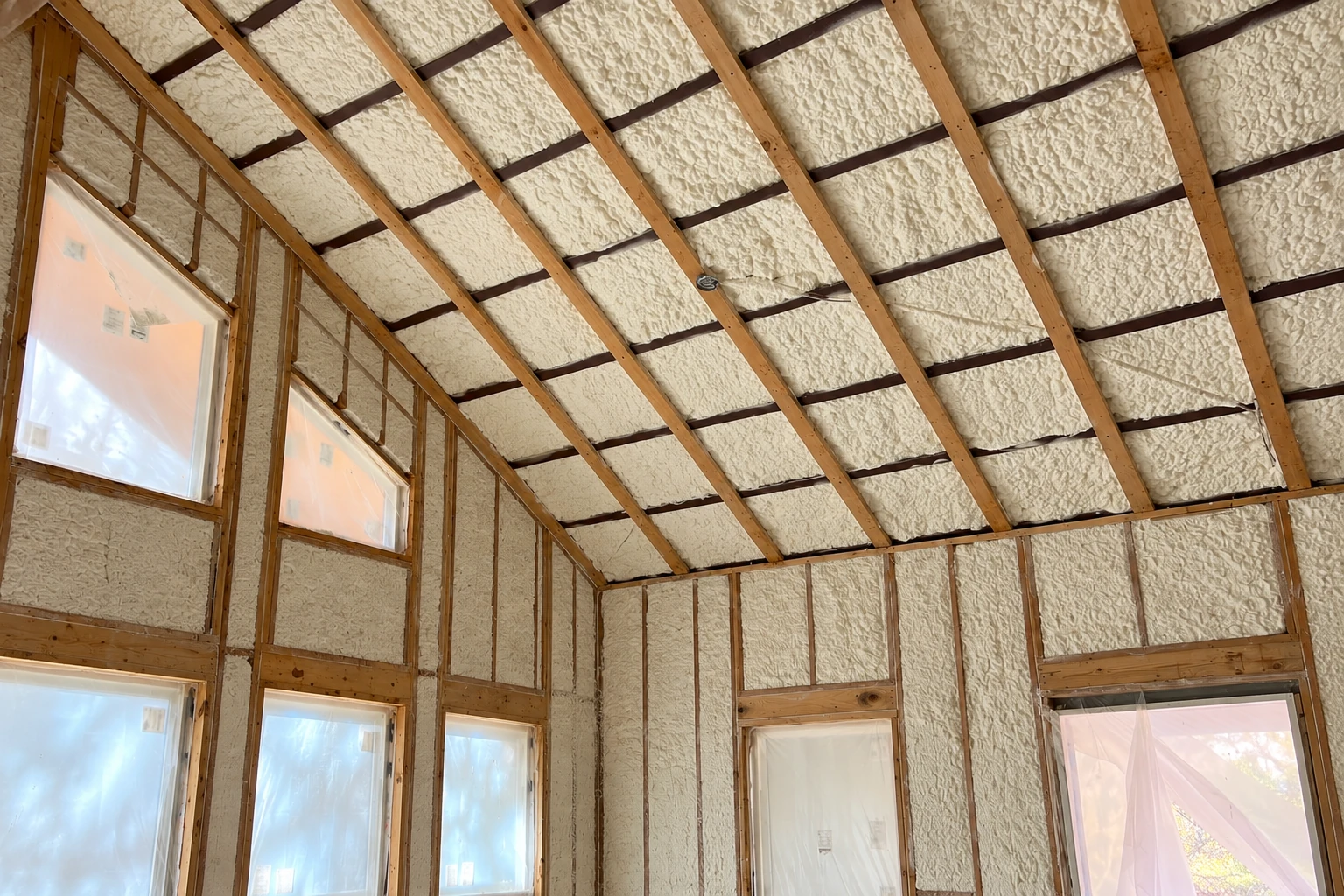 An unfinished attic with cream spray foam insulation between exposed roof rafters and wall studs.