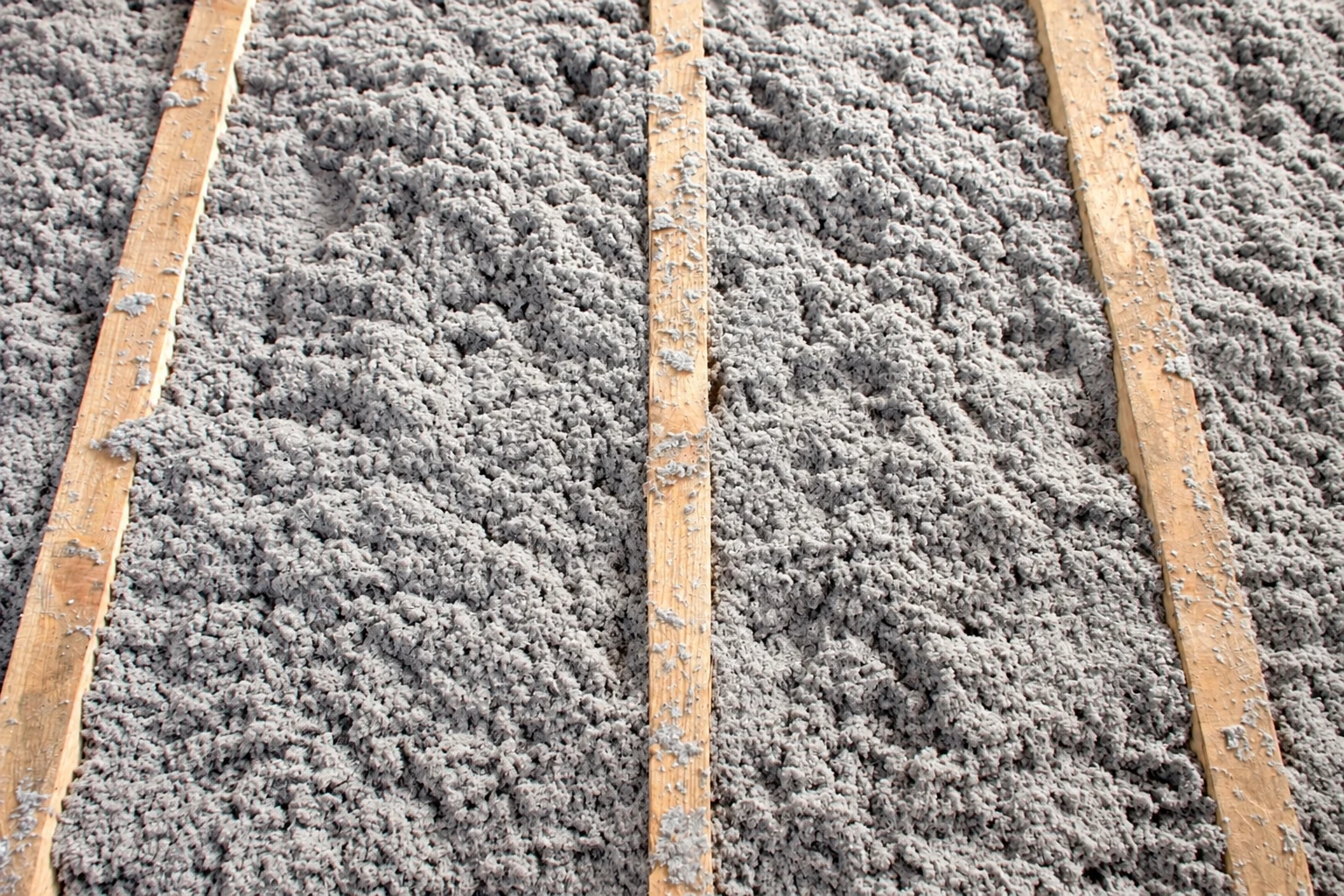 Gray blown-in insulation covers an attic floor between exposed wooden joists.