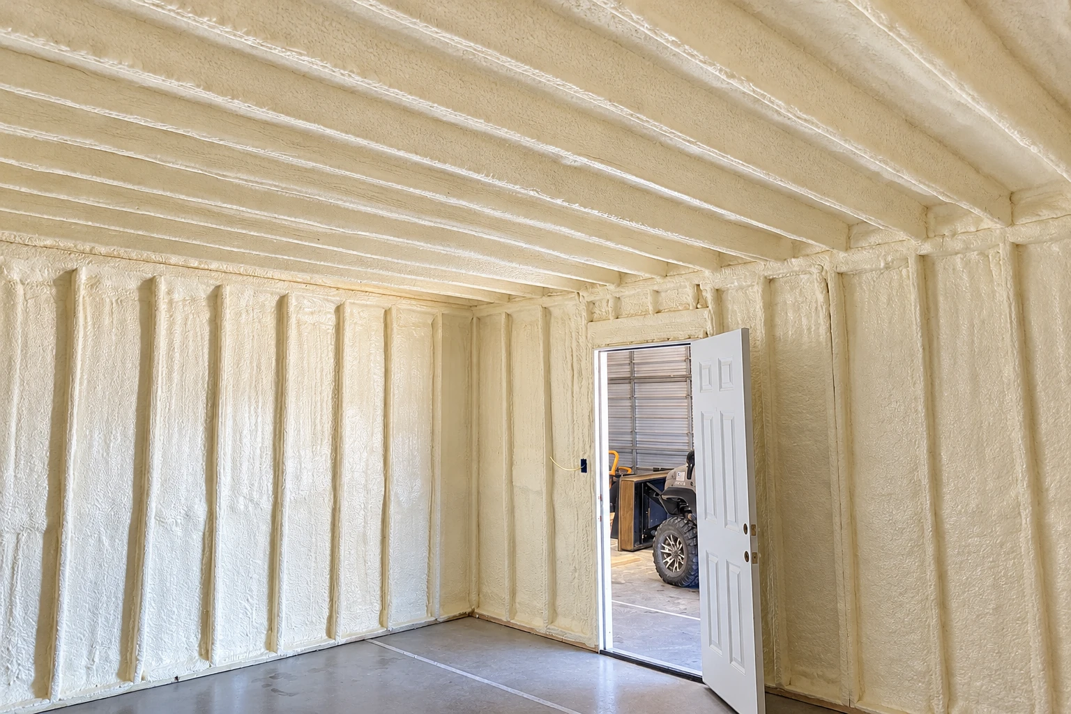 A commercial interior with cream-colored spray foam coating the walls and ceiling around an open doorway.