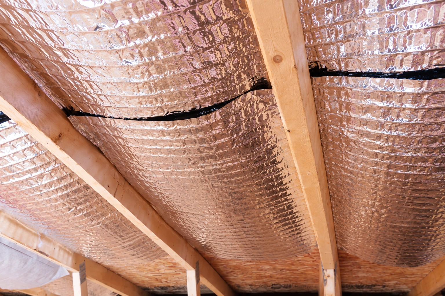 Reflective foil vapor barrier is installed between wooden ceiling joists.